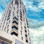 A modern high-rise building with a geometric facade against a backdrop of blue sky with clouds.