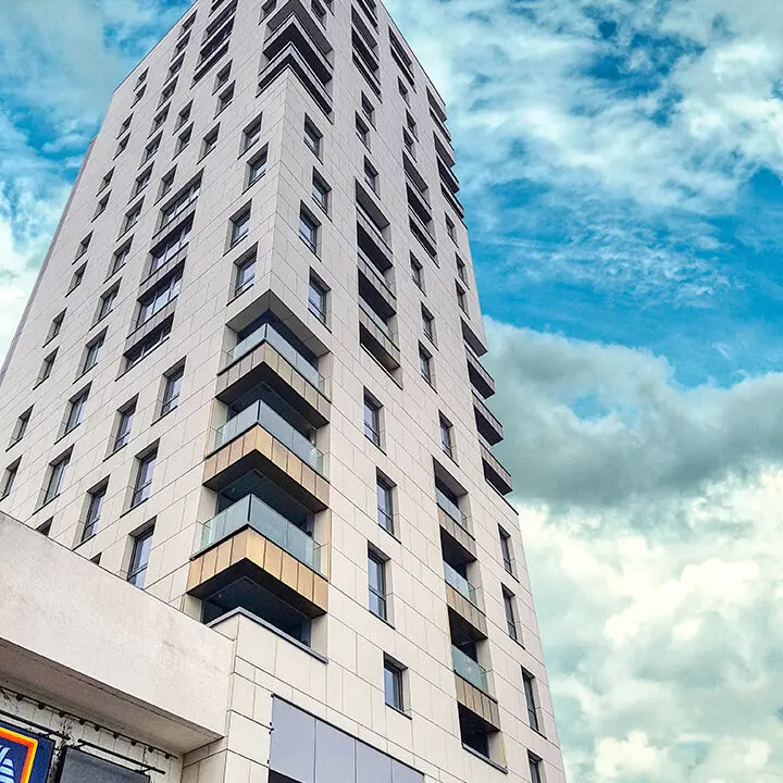 A modern high-rise building with a geometric facade against a backdrop of blue sky with clouds.