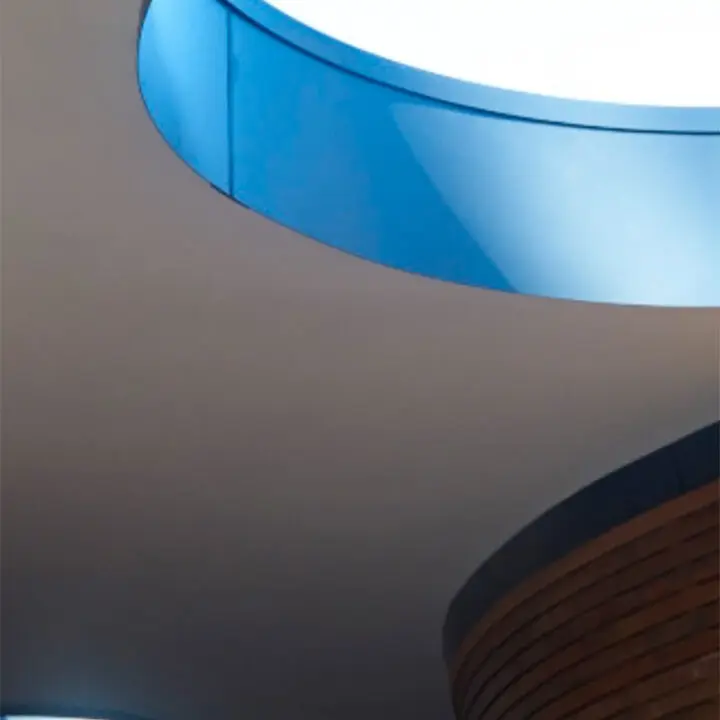 An interior view of a modern structure featuring a circular skylight with a blue tint and a section of curved wooden paneling, both accentuating the architectural design.