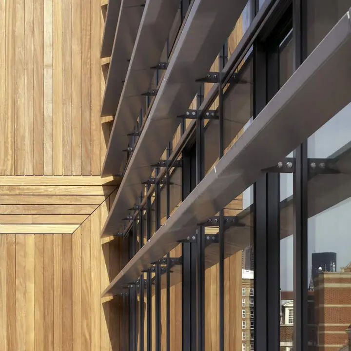 Modern building facade featuring wooden slats and reflective glass windows, with an urban skyline in the background.