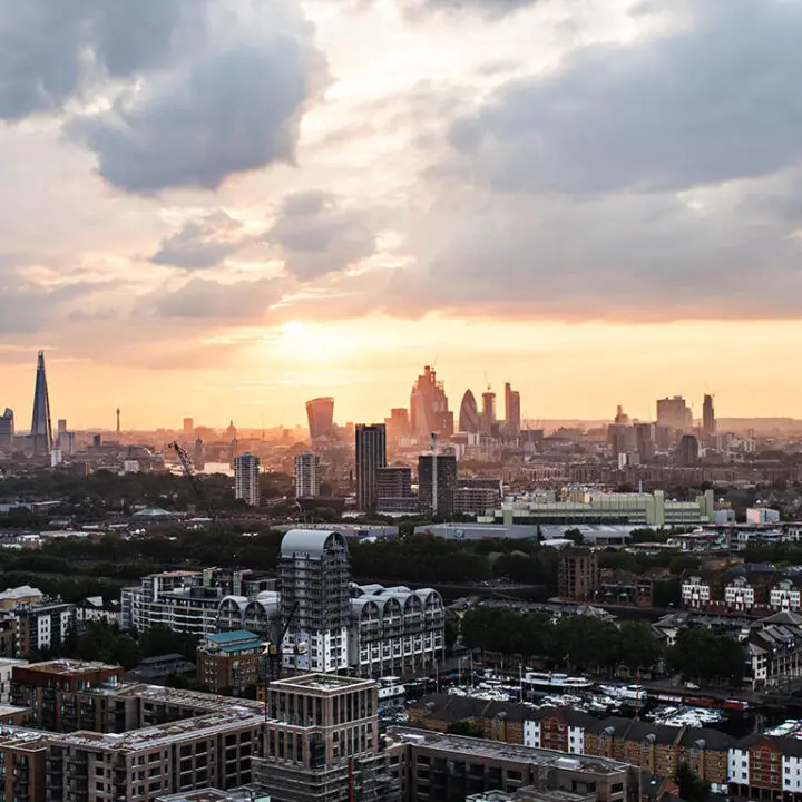 A cityscape at sunset, showcasing a mix of modern skyscrapers and residential buildings under a cloud-streaked sky.