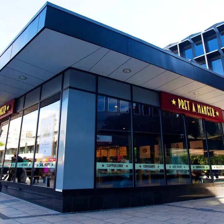 A modern storefront on a city street corner with large glass windows and a sign that reads "pret a manger.