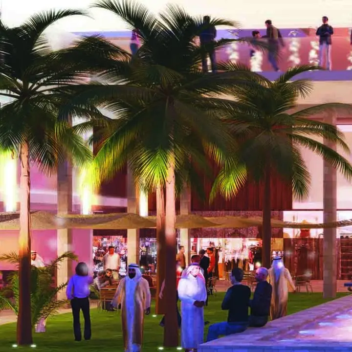A group of people gather around a brightly lit, modern outdoor setting with palm trees and a decorative fire feature in the evening.