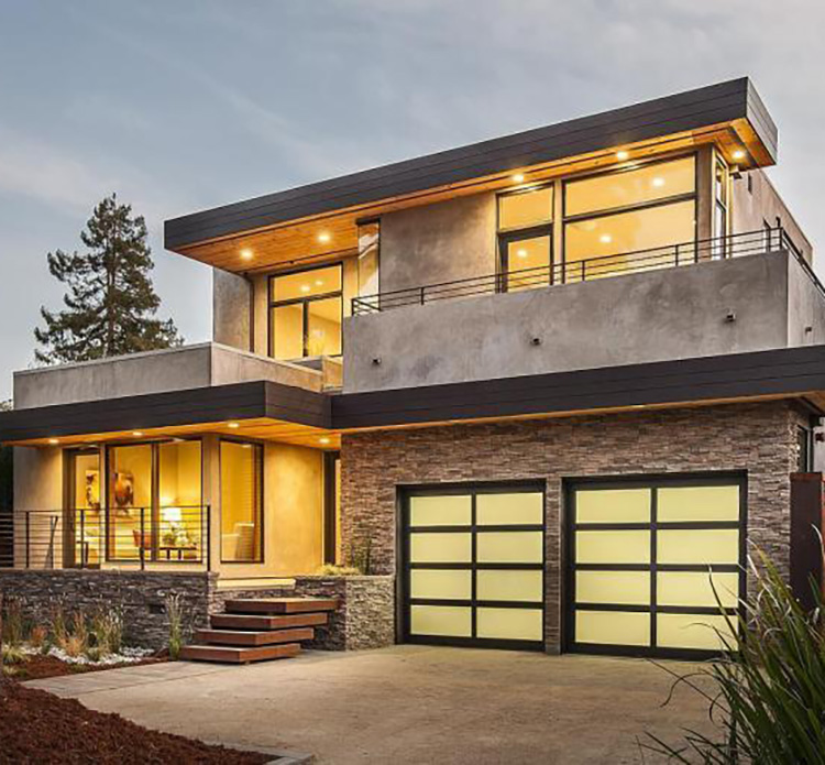 A modern two-story house with a flat roof, illuminated windows, and a double garage door at dusk.